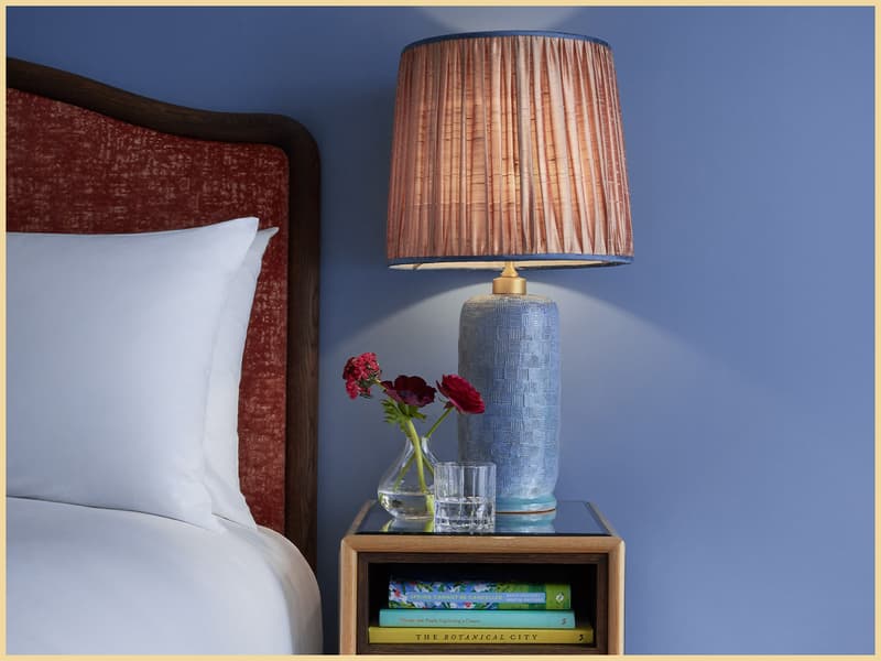 Blue Broadwick Soho bedroom with bedside lamp, red upholstered headboard and books.